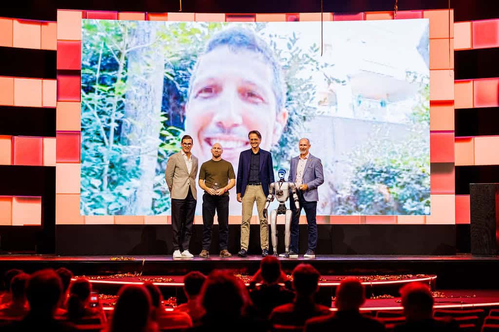 Futuristic AI robot and team presentation at AMLYZE event in front of large digital screen.