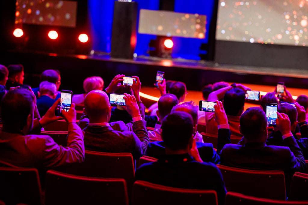 Smartphone users capturing a vibrant conference presentation on stage.