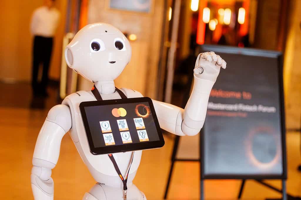 A friendly humanoid robot with a tablet on chest at an event venue.