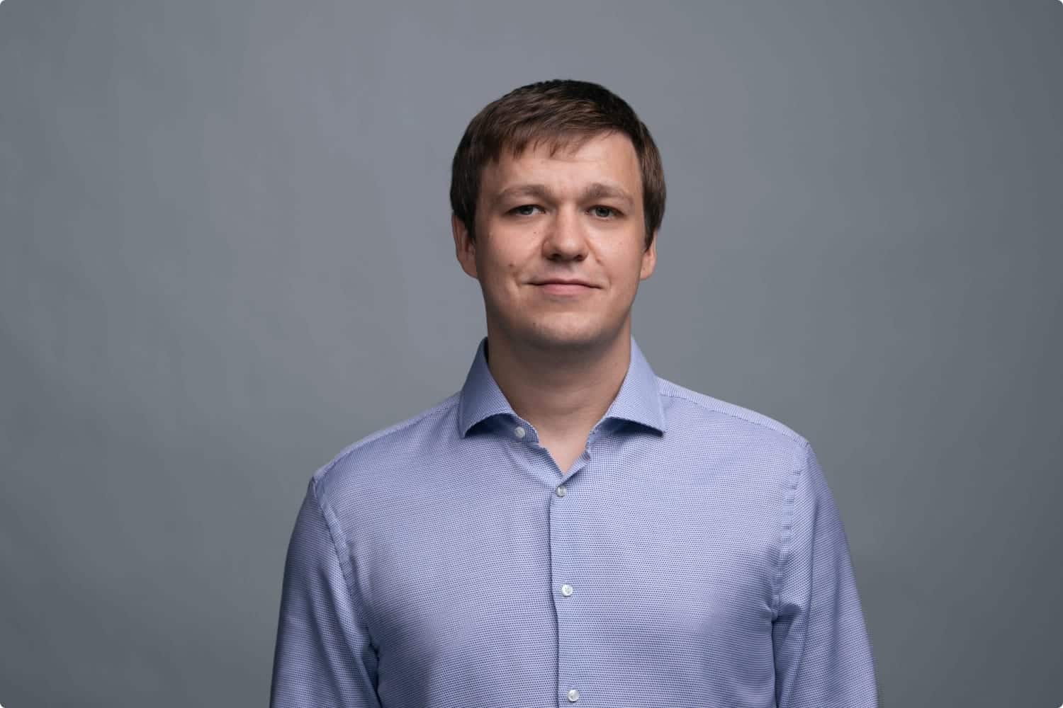 Professional young man in business attire looking at camera against gray background.